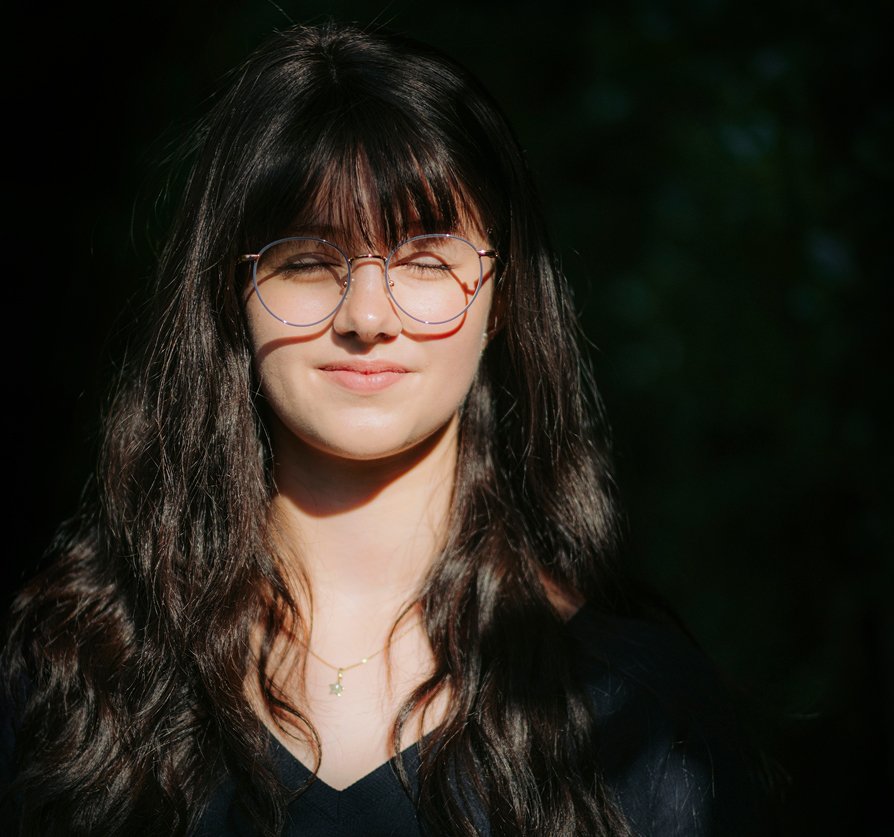 Frau mit langen, gewellten Haaren vor dunklem Hintergrund wird von der Sonne angeleuchtet.
